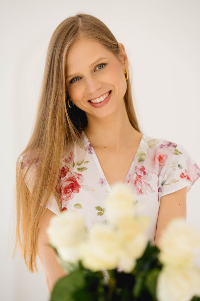 Autorka bloga Joanna Kotlicka ubrana w sukienkę w kwiaty, trzyma przed sobą bukiet białych róż.